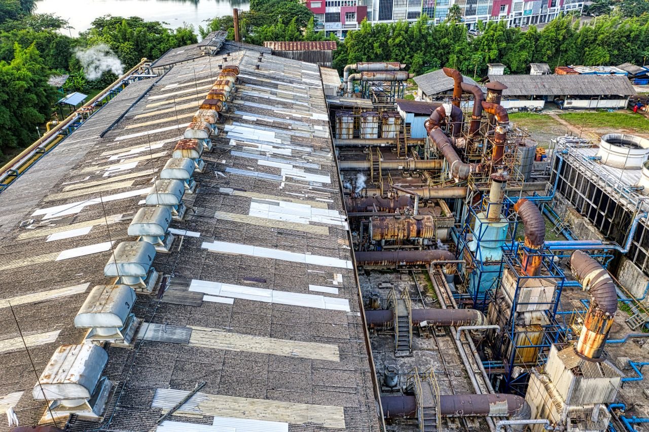 From above of industrial area of factory with large equipment placed in city among green trees in daylight